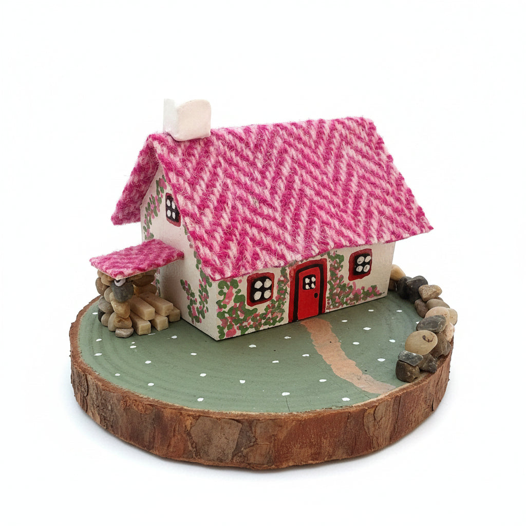 Small decorative house with a pink roof on a wooden base outdoors.