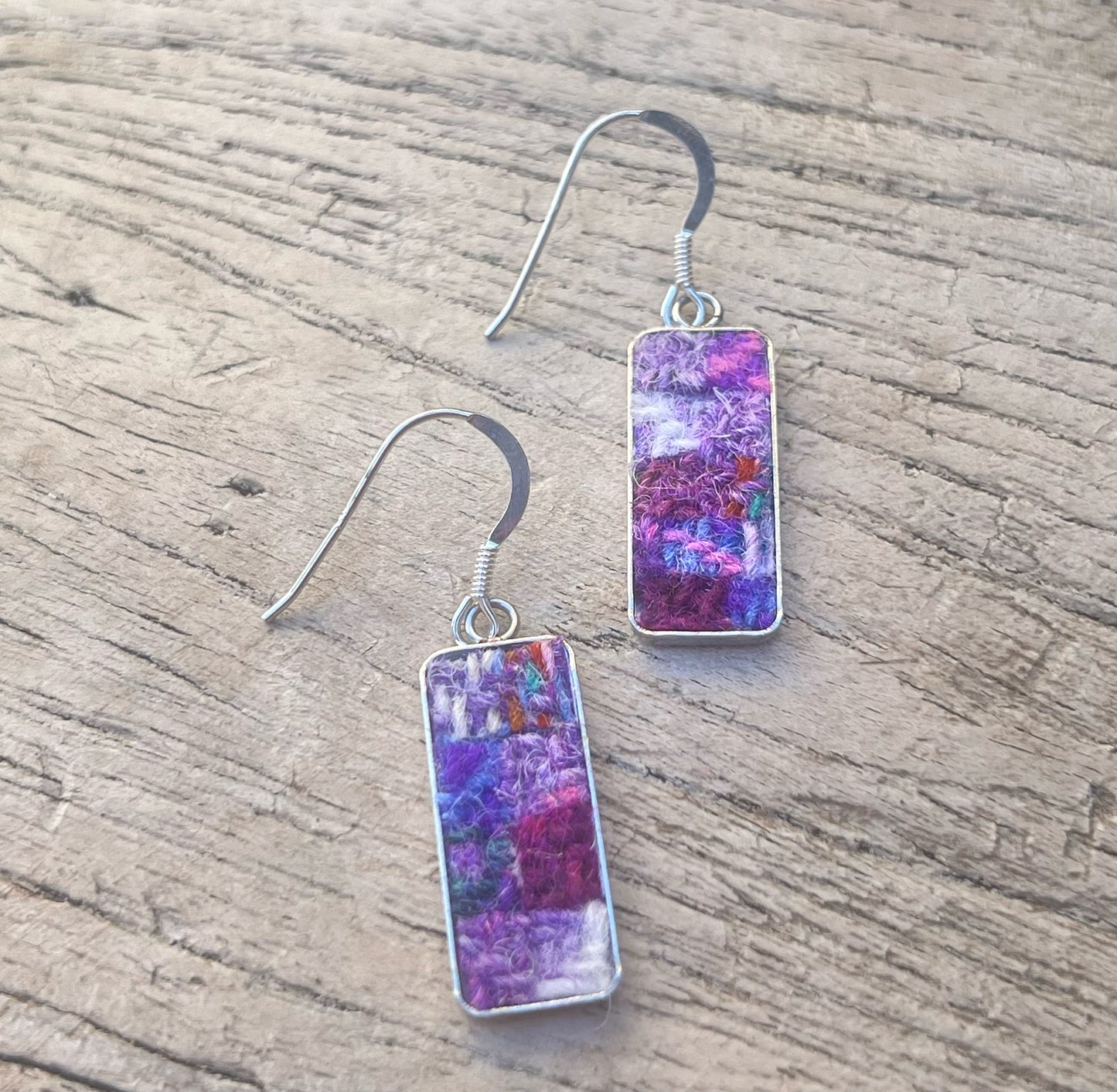 Pair of earrings with colorful rectangular stones on a wooden surface
