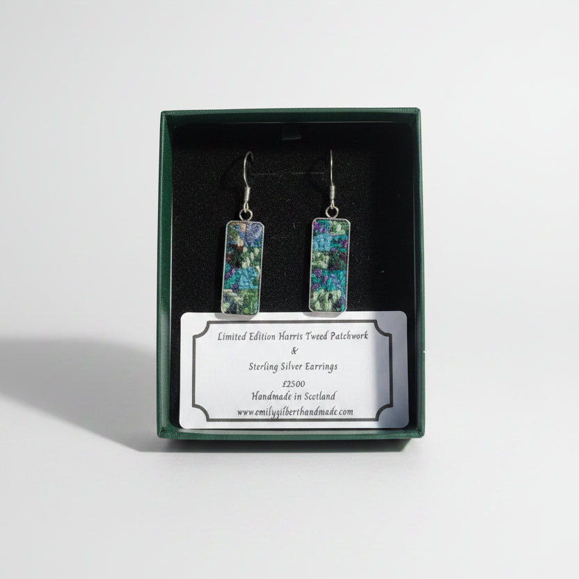 Pair of earrings in a green box with a label on a wooden surface