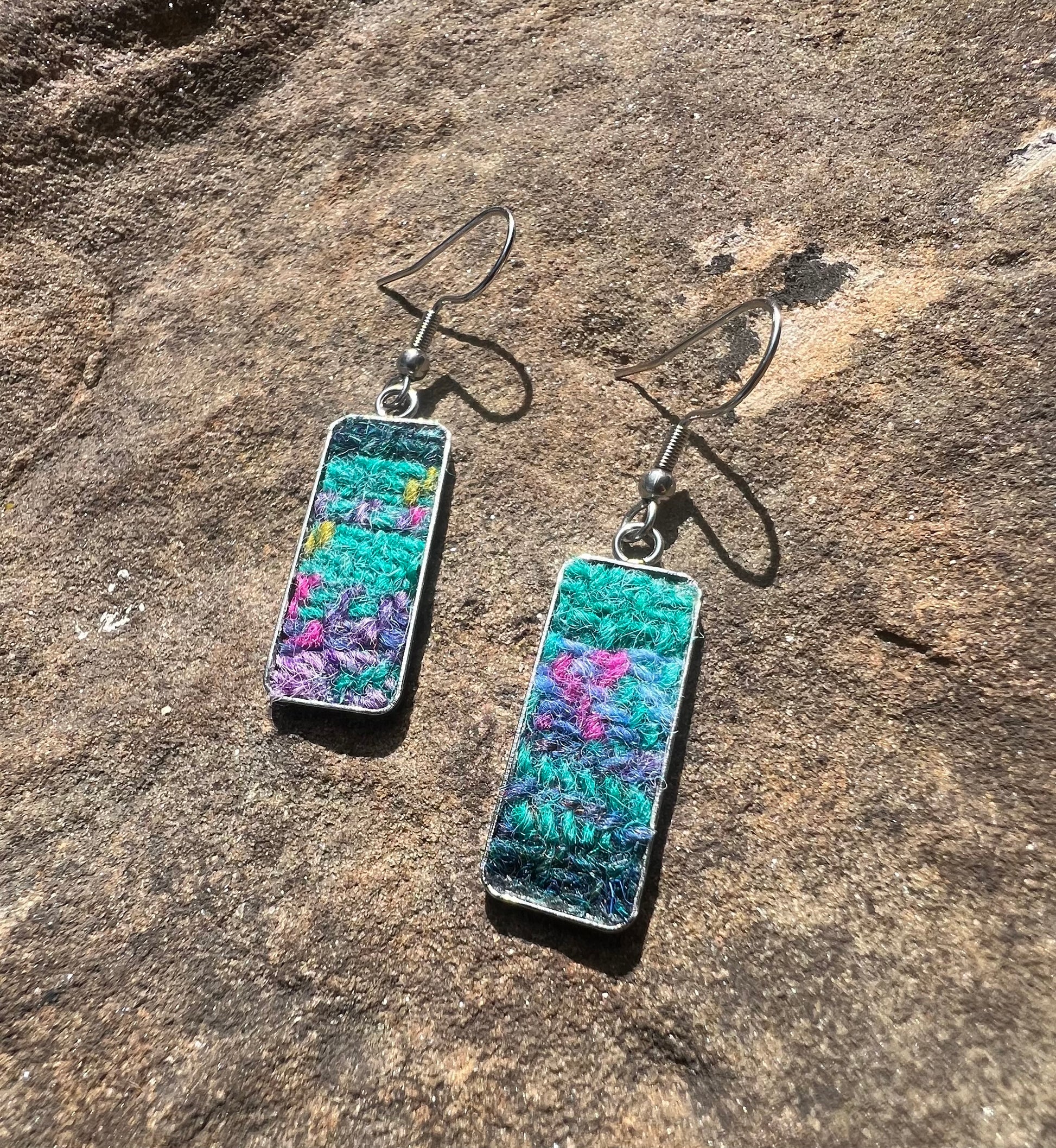 Pair of rectangular harris tweed patchwork earrings in teal, green, blue and pink on a stone surface