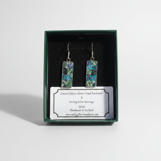 Pair of earrings in a green box with a label on a wooden surface